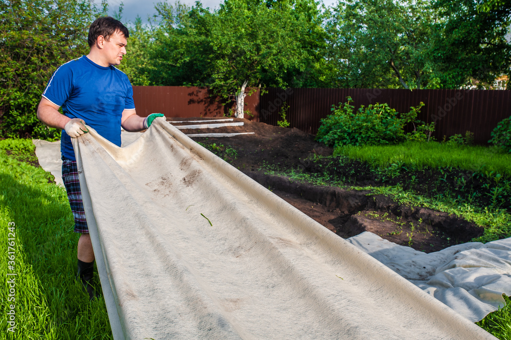 A man covers a dug hole with geotextile. Garden work, do-it-yourself pool A man covers a dug hole with geotextile. Garden work, do-it-yourself pool