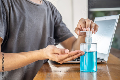 Closeup Asian man using hand sanitizer by pumping alcohol gel and washing before start to work with laptop in office period,Clear sanitizer in pump bottle, for killing germs, bacteria and virus