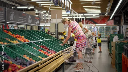 Wallpaper Mural A young woman in a protective mask on her face, during a pandemic, makes purchases in a supermarket. Choose food carefully. Retail at a large supermarket. Torontodigital.ca