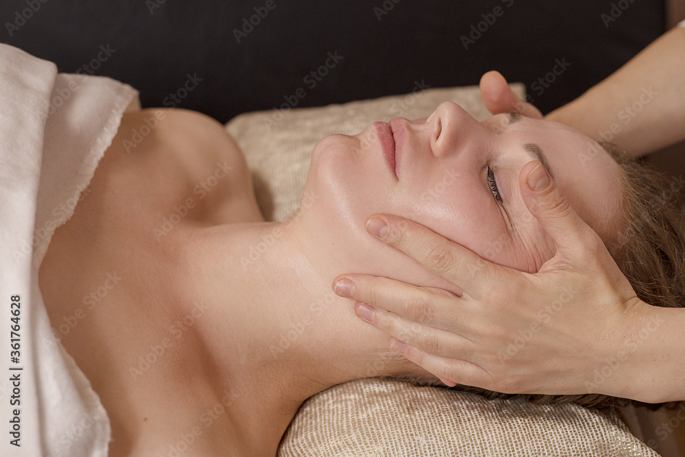 The hands of a masseur massage the face of a young woman in the salon. Professional care. Rejuvenating treatment. Anti age care. Cosmetology and medicine. The client is lying on the couch, side view