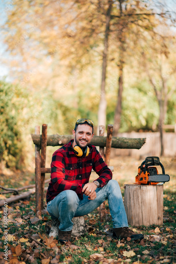 Portrait of a smiling young lumberjack sitting on a log in the woods on a sunny day. Portrait of a smiling young lumberjack sitting on a log in the woods on a sunny day.