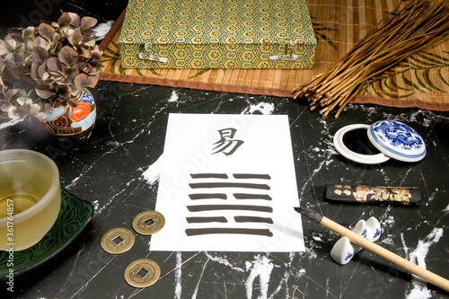 Close up of an I Ching arrangement with the 63th hexagram (After Completition/Chi Chi) written with a chinese ink brush on rice paper. There are also yarrow stalks and a chinese ink tank.