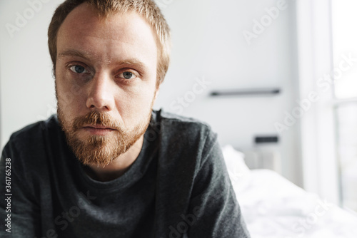 Photo closeup of redhead man looking at camera while sitting on bed