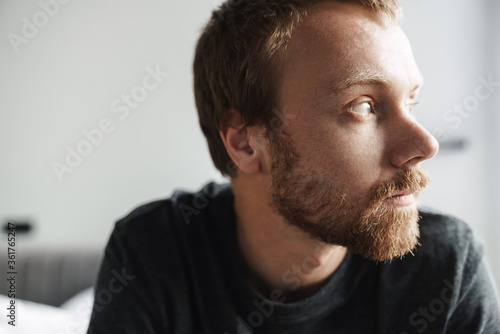 Photo closeup of redhead man looking aside while sitting on bed