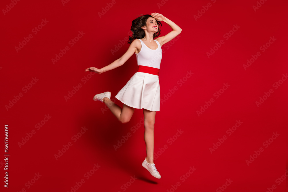 Full size profile photo of funny crazy lady jumping high up good mood rejoicing look far away hand help eyes see better wear white short dress shoes isolated red color background Full size profile photo of funny crazy lady jumping high up good mood rejoicing look far away hand help eyes see better wear white short dress shoes isolated red color background