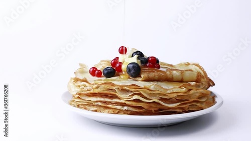 Tasty pancake or crepes with berries and honey. Honey or Maple syrup is poured on pancakes. Tasty and sweet breakfast concept with pancakes and berries