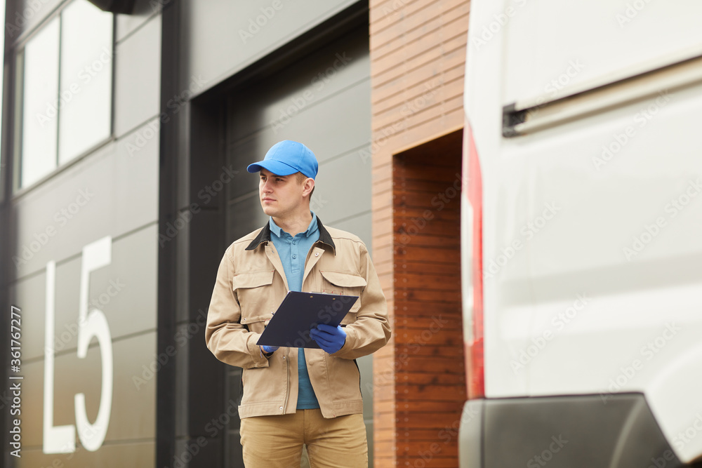Young delivery person in uniform working with loads in warehouse outdoors Young delivery person in uniform working with loads in warehouse outdoors