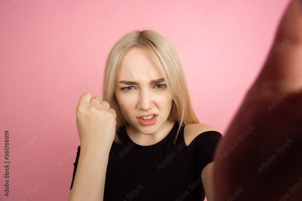 Selfie view. Portrait of young caucasian woman with bright emotions on coral pink studio background. Blonde female model. Concept of human emotions, facial expression, sales, advertising, youth. Selfie view. Portrait of young caucasian woman with bright emotions on coral pink studio background. Blonde female model. Concept of human emotions, facial expression, sales, advertising, youth.