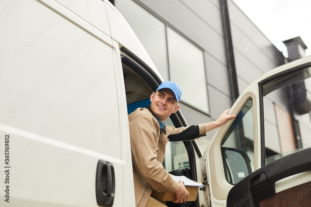 Young smiling courier holding package while sitting in the van he delivering parcels Young smiling courier holding package while sitting in the van he delivering parcels