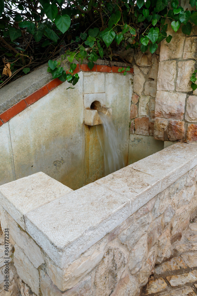The small decorative fountain - waterfall in the territory of the Blumfield public park in the light of the rays of the setting sun in Jerusalem, Israel