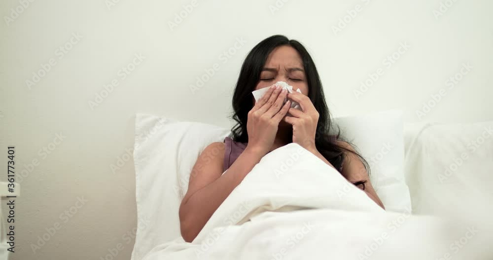 Asian woman sneeze and has sick, Thai girl has cold and illness and lay down on bed in bedroom Asian woman sneeze and has sick, Thai girl has cold and illness and lay down on bed in bedroom