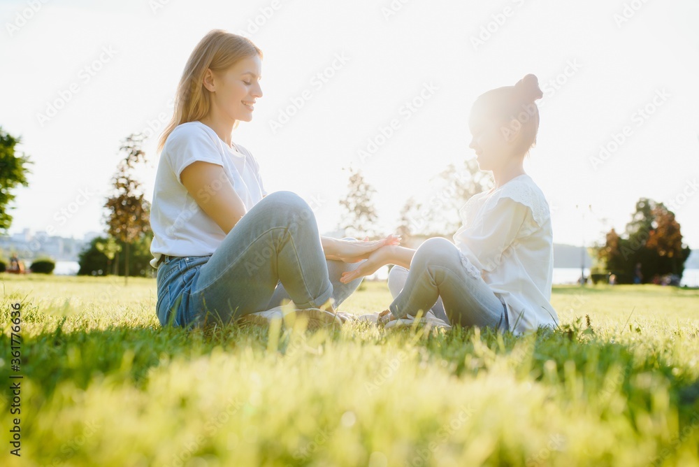Happy mother and daughter relaxing in the park. Beauty nature scene with family outdoor lifestyle at spring or summer time. Happy stylish family resting together, having fun outdoor. - obrazy, fototapety, plakaty 