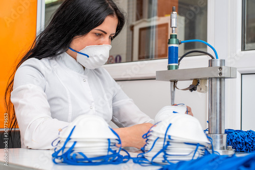 A woman works at a machine for the manufacture of medical masks with nanofibre and solder loops to them with ultrasound. Coronovirus and Covid-19 Prevention photo