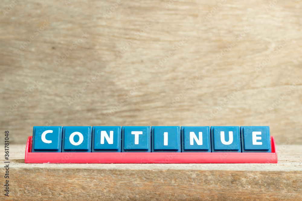 Tile letter on red rack in word continue on wood background Tile letter on red rack in word continue on wood background