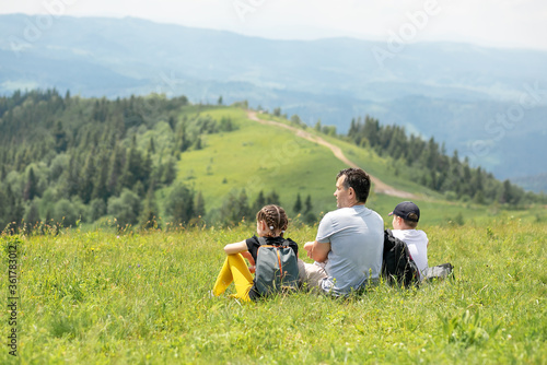 Father and children are sitting on the top of the mountain and looking into the distance.