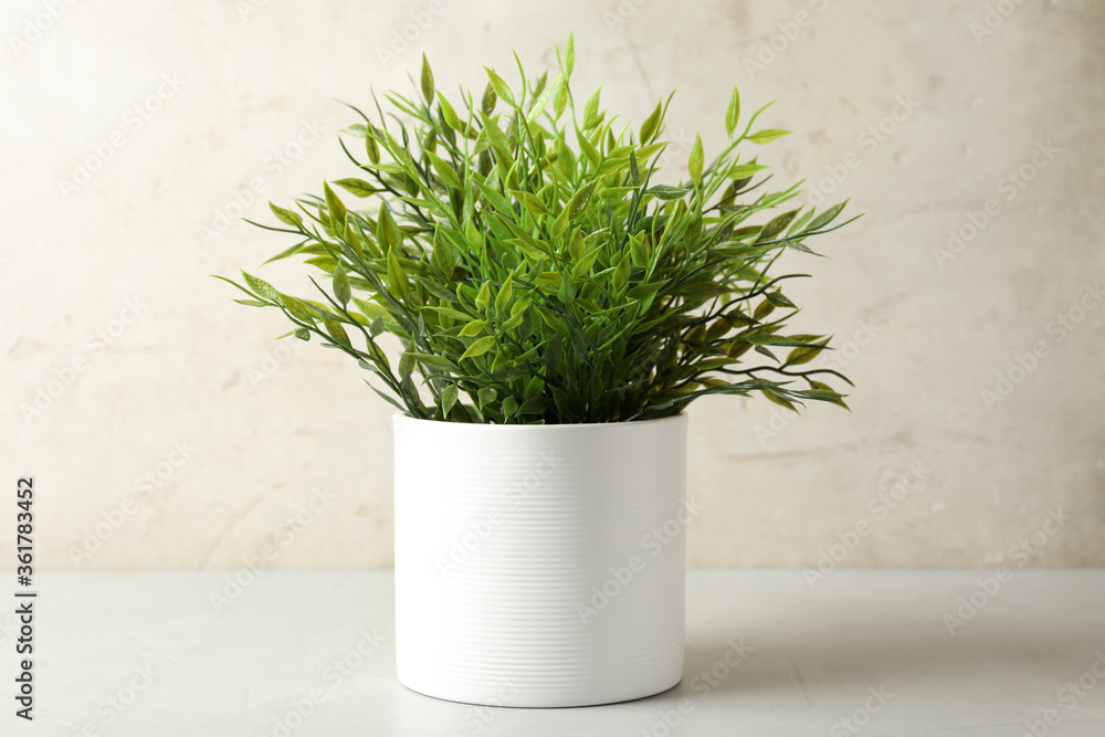 Artificial plant in white flower pot on table against light background Artificial plant in white flower pot on table against light background