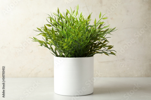 Artificial plant in white flower pot on table against light background