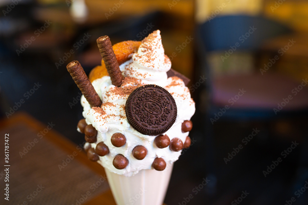 Cool milkshake with cookies and chocolate balls. Milkshake in a glass beaker on a table on a street platform in a cafe. Refreshing summer drinks