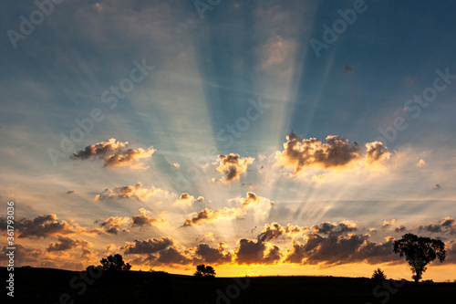 Photography Sunrays during a sunrise with clouds, a blue sky, and black landscape