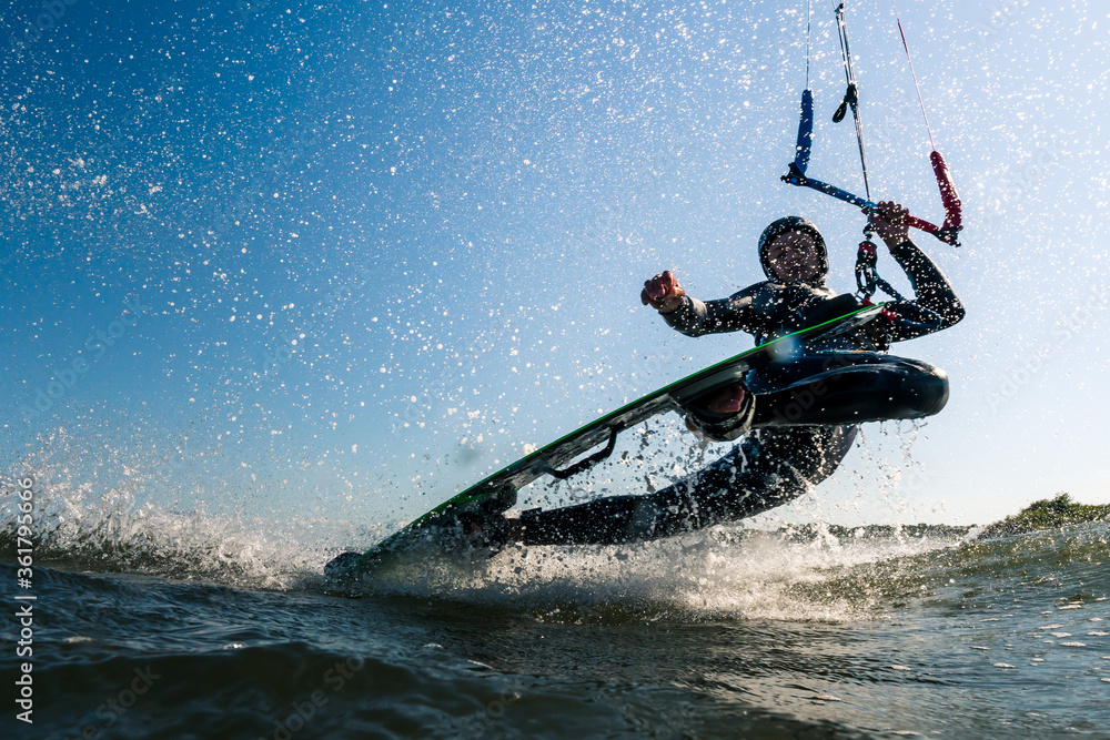 Obraz premium Kitesurfer doing an impressive darkslide trick with lots of spray water