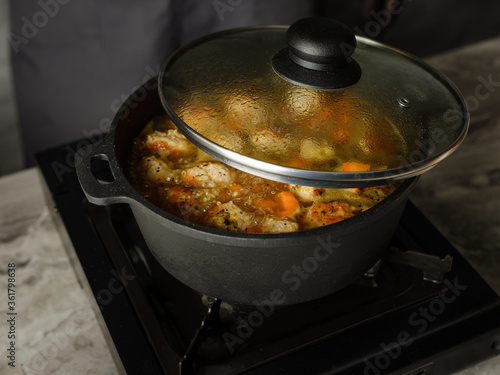 Cooking soup with meatballs cutlets and vegetables in big pan pot on home kitchen background by chef hands. Copy space, closeup. Homemade food recipe concept.