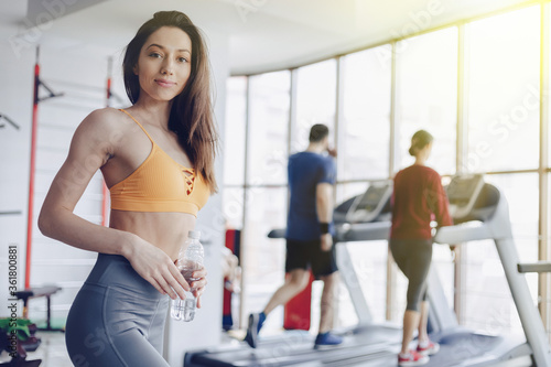 Fototapeta Naklejka Na Ścianę i Meble -  young attractive girl in the gym drinking water on the background of treadmills