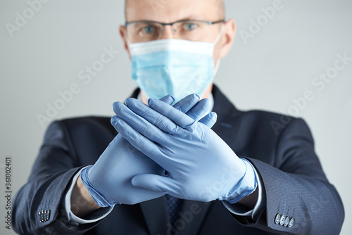 Prohibition sign in focus. A businessman in medical mask and rubber gloves in blur shows prohibition sign with both hands.