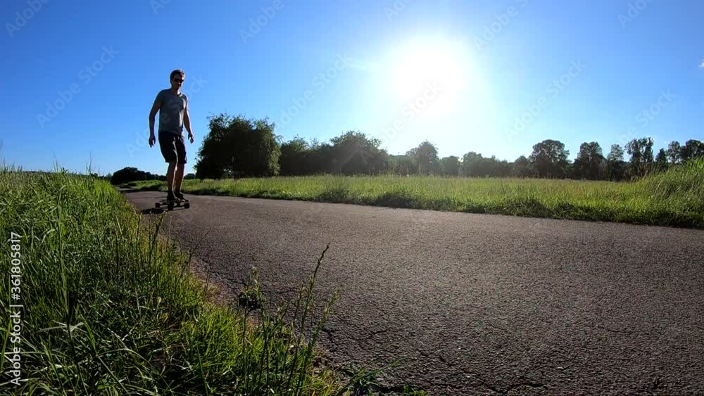Slow motion shot of skateboarder performing a breaking manoeuvre on his longboard on a rural road during a scenic sunset (front-view) Slow motion shot of skateboarder performing a breaking manoeuvre on his longboard on a rural road during a scenic sunset (front-view)