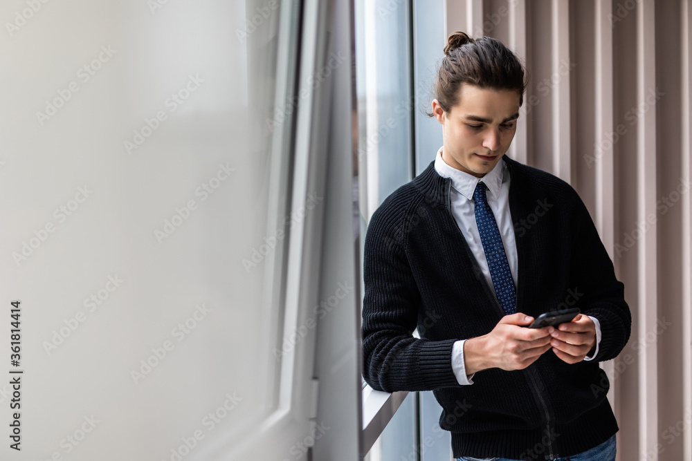 Enjoying office life. Joyful young man holding mobile phone and looking at camera on office background Enjoying office life. Joyful young man holding mobile phone and looking at camera on office background