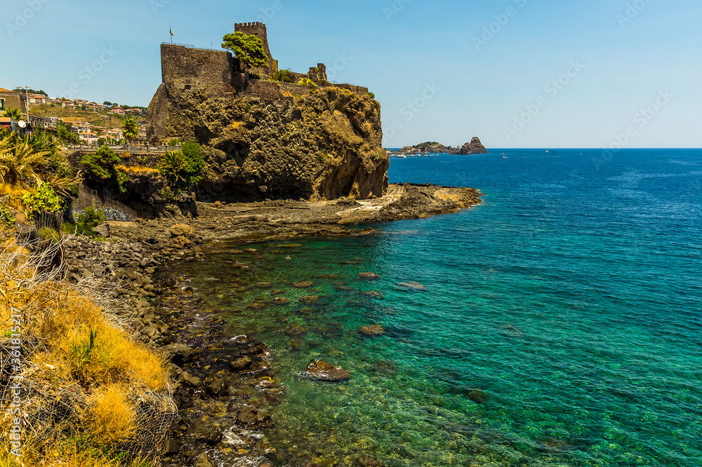A view along the seafront in Acicastello, Sicily showing the Norman castle and the islets of Acitrezza in summer