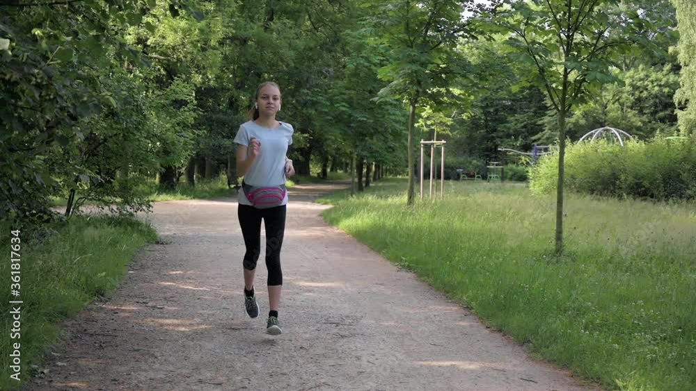 Slow motion shot of girl runs in summer in park. Healthy lifestyle concept. Female child with headphones listening music is engaged in fitness. Slow motion shot of girl runs in summer in park. Healthy lifestyle concept. Female child with headphones listening music is engaged in fitness.