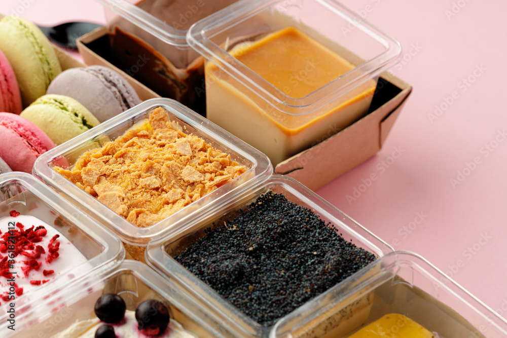 Mousse desserts in square plastic boxes with different toppings on pink table Mousse desserts in square plastic boxes with different toppings on pink table