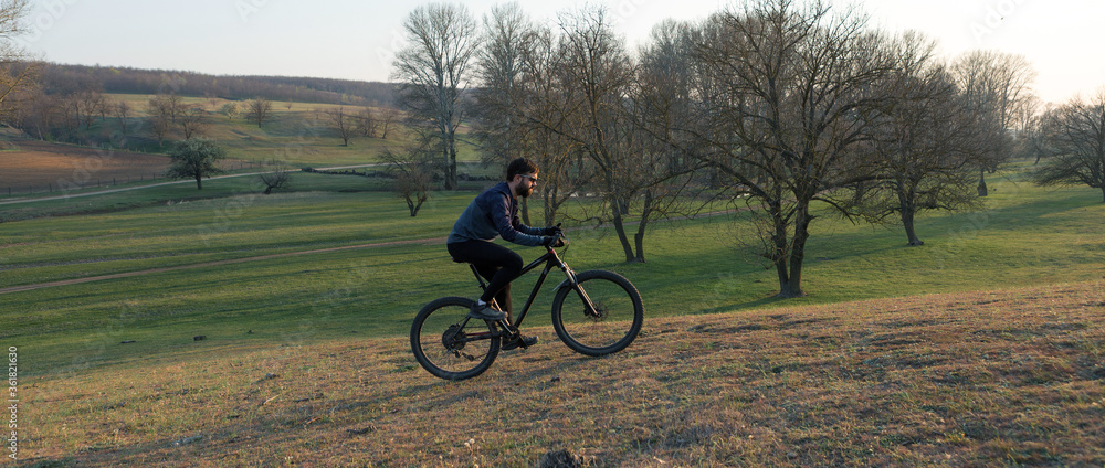 Fototapeta premium Cyclist in shorts and jersey on a modern carbon hardtail bike with an air suspension fork standing on a cliff against the background of fresh green spring forest