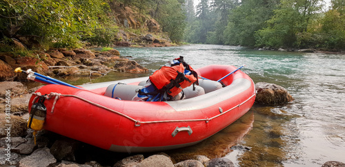 Red raft on edge of beautiful river with backpack and ores resting inside