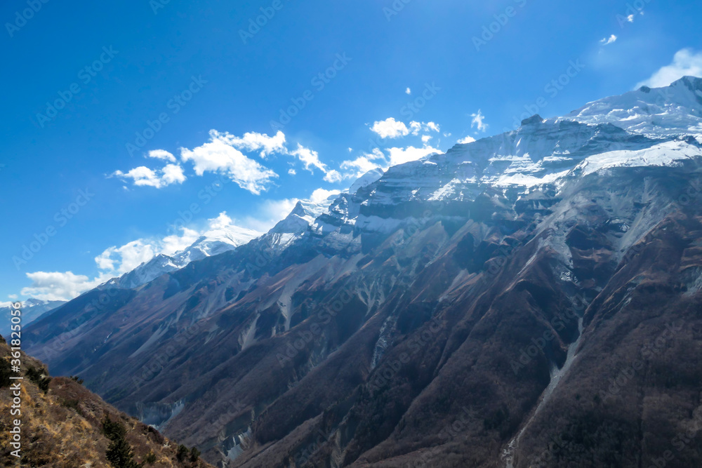 A panoramic view on sharp and dangerous, high, snow capped Himalayan peaks long Annapurna Circuit in Nepal. Slopes are overgrown with small bushes. Exploration and discovering. Steep mountain wall.