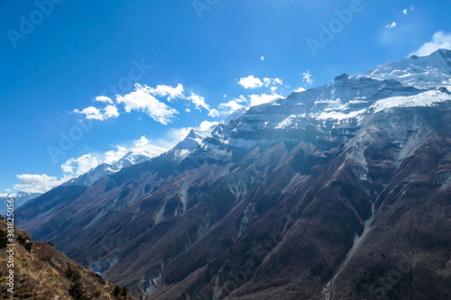 A panoramic view on sharp and dangerous, high, snow capped Himalayan peaks long Annapurna Circuit in Nepal. Slopes are overgrown with small bushes. Exploration and discovering. Steep mountain wall. © Chris