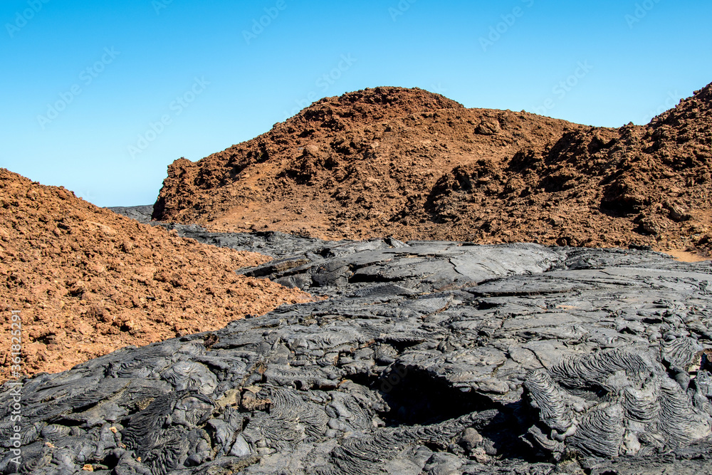 A black lava flow contrasts with the red soil of the hills of Santiago Island in the Galapagos Islands