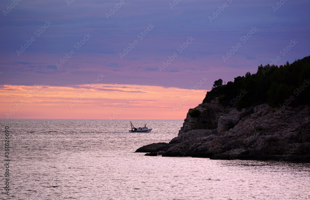 Pink, violet and indigo blue color tone sea sunset with fishing boat on the horizon