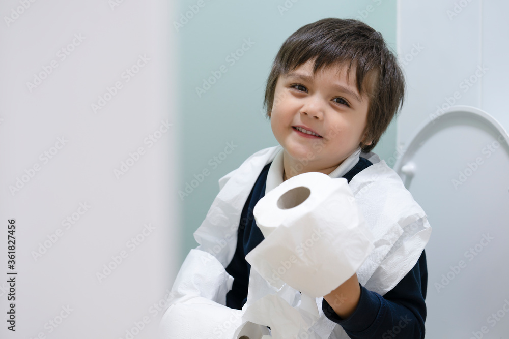 School boy playing with tiolet rolls while learning how to clean him self, Healthy child happy sitting in the toilet on his own and playing with the tissues, Training child or Health care concept. School boy playing with tiolet rolls while learning how to clean him self, Healthy child happy sitting in the toilet on his own and playing with the tissues, Training child or Health care concept.