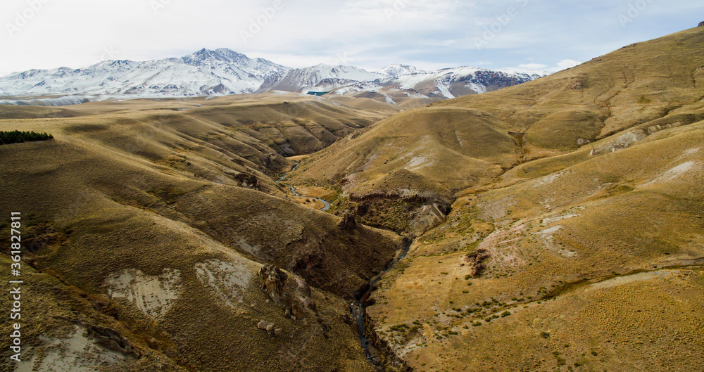 Obraz premium Rural landscape. Steep cliffs and yellow meadow. Aerial view of the river flowing along the golden valley in the mountains. 