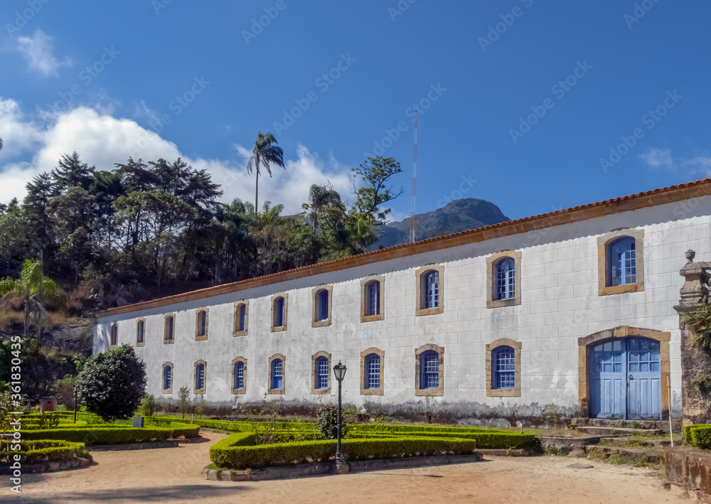 Old two-story building, from the colonial period, with beautiful garden in front and forest in the background, blue sky, Caraca Sanctuary, city of Catas alta, state of Minas Gerais, Brazil