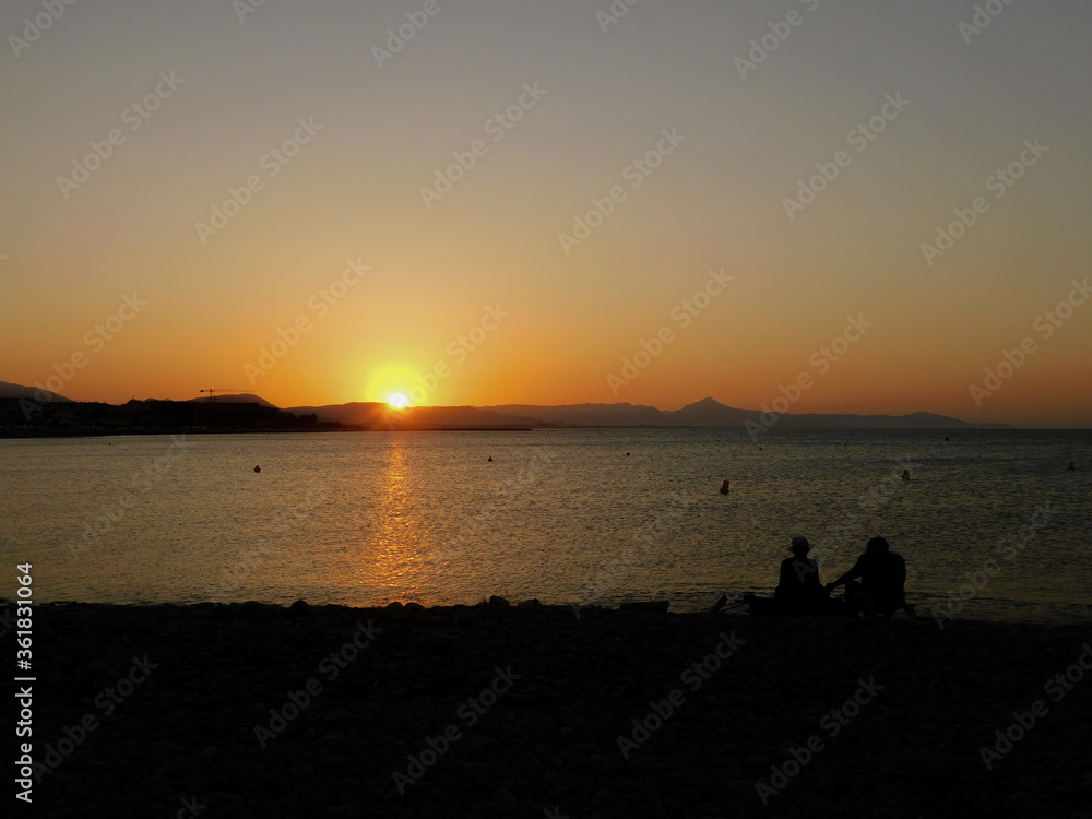 A couple looking at the sunset on a rockbeach. Two people looking the sundown on a beach