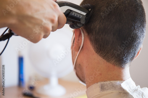 Cutting hair to young boy with mask coronavirus, hairdresser hand with machine 