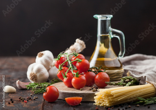 Raw spaghetti pasta with cherry tomatoes, olive oil with garlic and rosemary on wooden background.