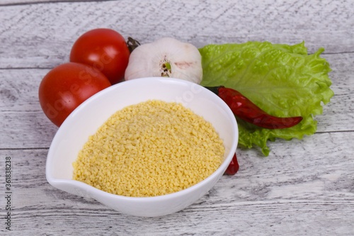 Raw couscous in the bowl served salad leaves, tomato and pepper photo