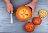 Men's hands with a knife cut a pumpkin on a gray wooden table. Halloween concept