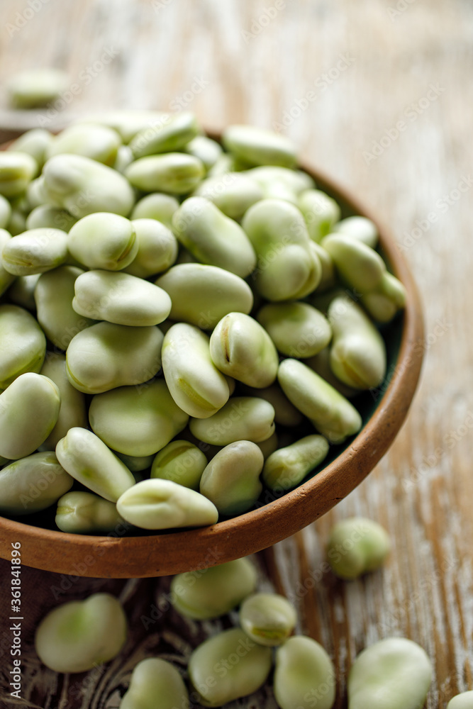 Fresh broad beans in a ceramic bowl on a wooden table close up view Fresh broad beans in a ceramic bowl on a wooden table close up view