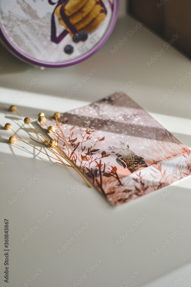 A postcard on the table, on which the rays of the sun are softly falling, in the background there is a box of cookies, the photo is great for personal pages and websites A postcard on the table, on which the rays of the sun are softly falling, in the background there is a box of cookies, the photo is great for personal pages and websites