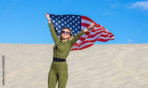 Foto Blond woman with USA flag against blue sky and sandy beach proclaims America Independence Day
