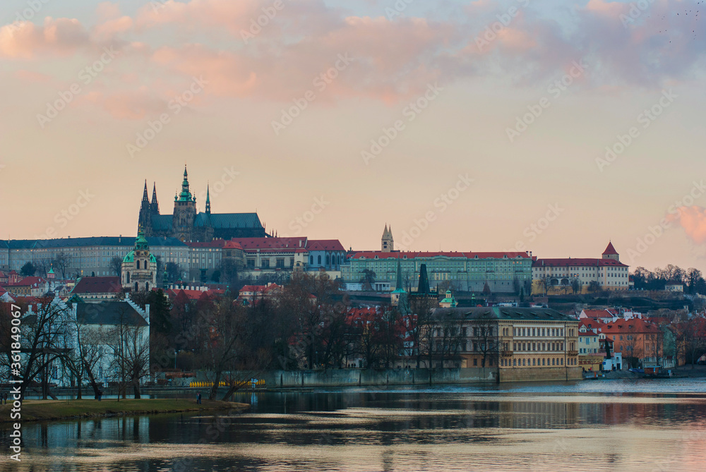 Panorama of Prague, Czech Republic at sunset. View of St. Vitus Cathedral from afar, buildings on the embankment of the Vltava River in the foreground.